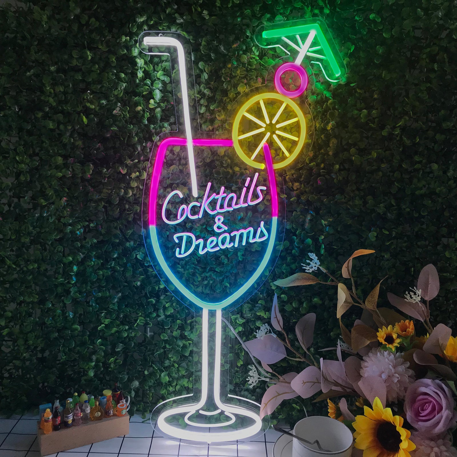 Cocktails & Dreams mini neon sign glowing brightly above a green shelf with liquor bottles in a cozy bar setting.