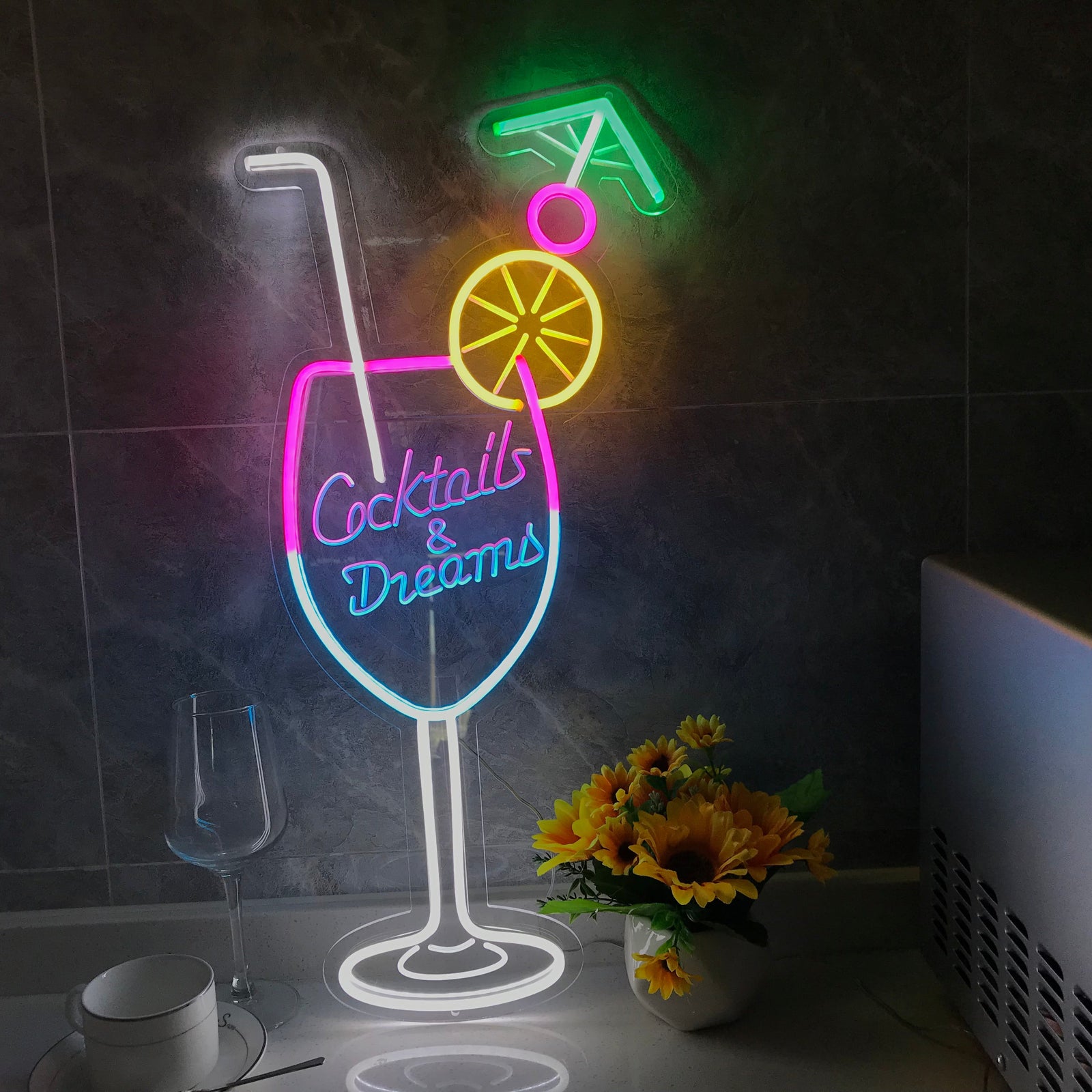 A close-up shot of the illuminated Cocktails & Dreams mini neon sign on a tiled wall next to a kitchen counter.