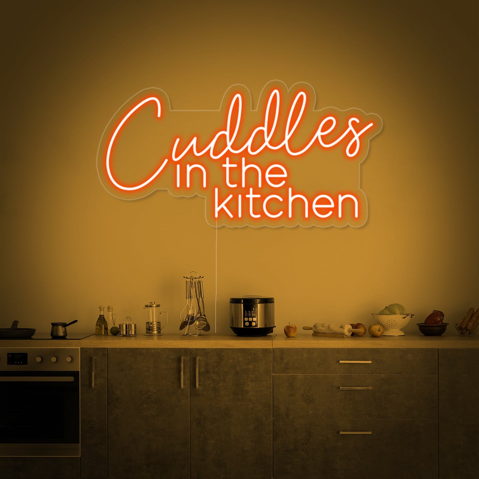 The 'Cuddles in the Kitchen' neon sign illuminates a cozy modern kitchen counter, creating a warm ambiance next to a mug and cookbook.