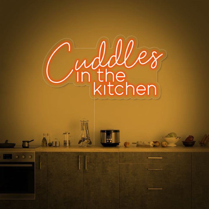 The 'Cuddles in the Kitchen' neon sign illuminates a cozy modern kitchen counter, creating a warm ambiance next to a mug and cookbook.
