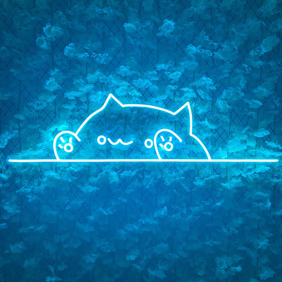 A charming, stylized glow of a sitting kitten neon sign, illuminated in warm white and pinkish-orange hues, casting a soft light in a cozy modern living room above a plush armchair.