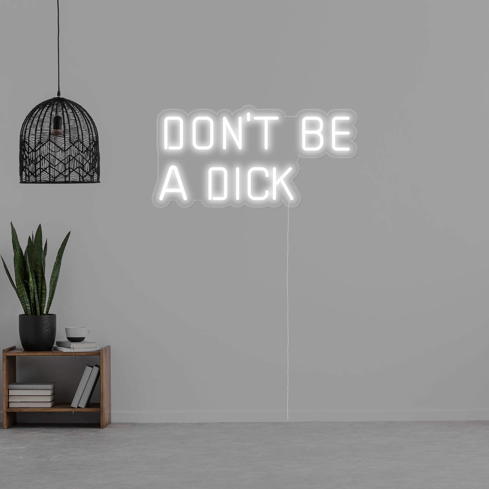 The actual 'Dont Be a Dick' neon sign, glowing in white tubing with visible clear wiring and backing, photographed in a workshop context.