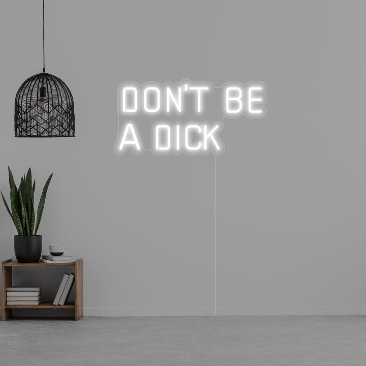 The actual 'Dont Be a Dick' neon sign, glowing in white tubing with visible clear wiring and backing, photographed in a workshop context.