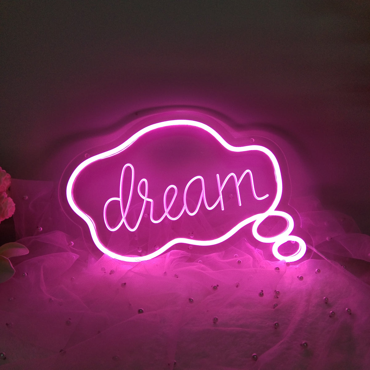 "Dream" USB Mini LED Neon Sign illuminated in pink, showing the 3D engraved letters and silicone neon strip on an acrylic backer resting on a textured fabric surface.