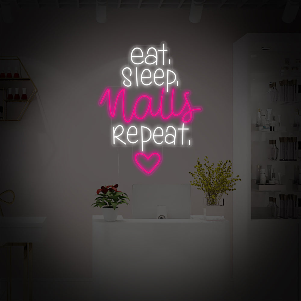A vibrant glowing neon sign with the text Eat Sleep Nails Repeat in stylized light blue and pink lines, accompanied by simple icons of a plate with cutlery, a crescent moon, and a polished fingernail. The neon sign is mounted on an exposed brick wall above a clean, modern reception desk with nail polishes and plants in a well-lit salon environment.