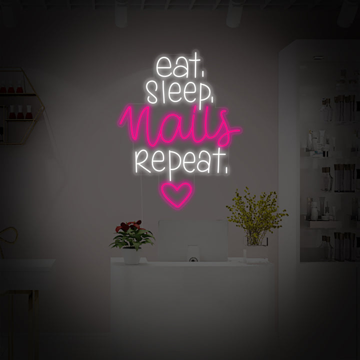 A vibrant glowing neon sign with the text Eat Sleep Nails Repeat in stylized light blue and pink lines, accompanied by simple icons of a plate with cutlery, a crescent moon, and a polished fingernail. The neon sign is mounted on an exposed brick wall above a clean, modern reception desk with nail polishes and plants in a well-lit salon environment.
