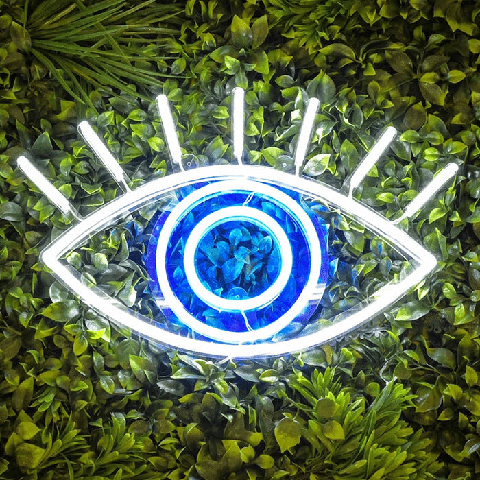 Modern glowing 'Element Symbol Eye' neon wall decor mounted on an artificial green leaf wall, creating an artistic and alternative vibe.