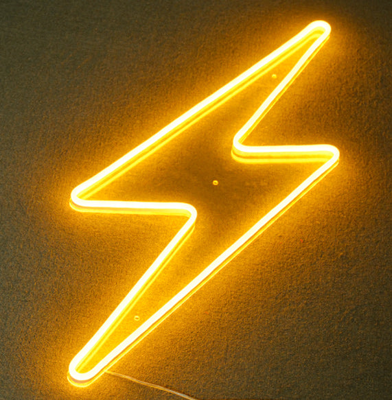 Real neon sign featuring an E element symbol combined with a glowing blue lightning bolt, mounted on a wall above a desk with office items and plants.