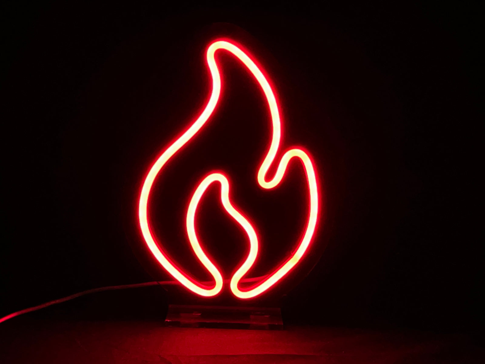 Closeup of the 'Fire' desk neon light on a wooden shelf next to home decor.