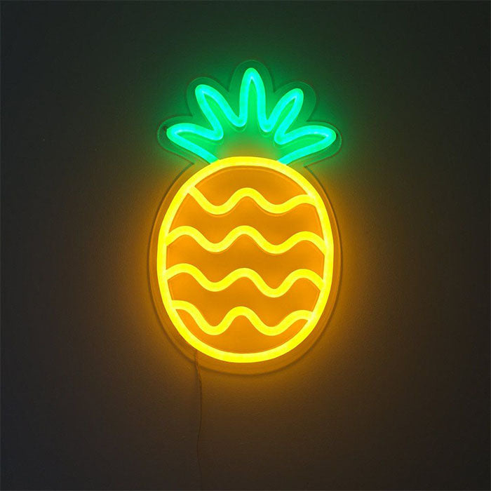 A real pineapple neon sign glowing yellow and green on a textured wall