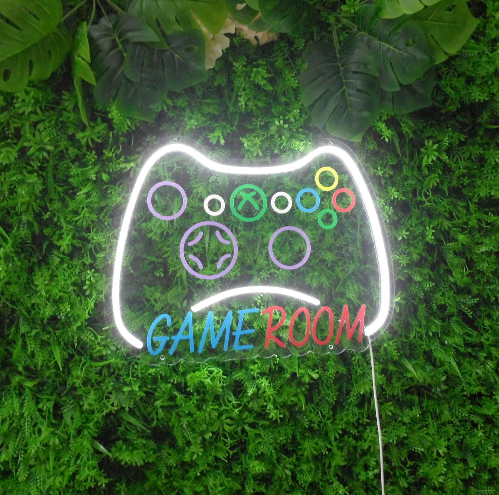 A physical, glowing game controller neon sign mounted on a green wall, featuring distinct colored buttons and wiring details.