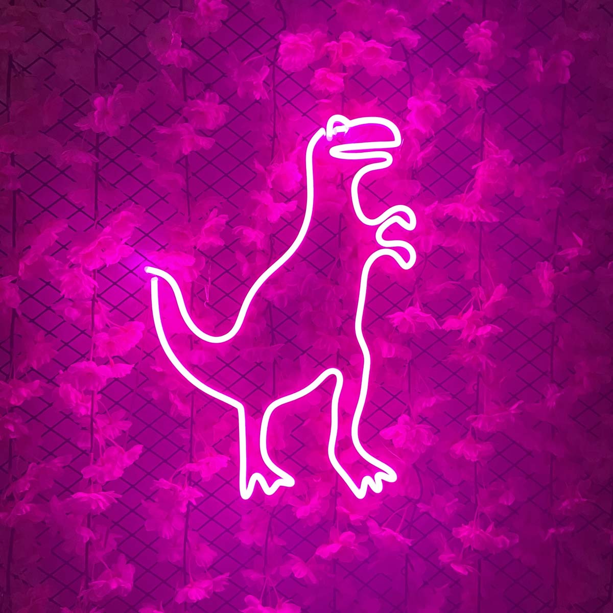 A vibrant neon sign depicting the Godzilla monster silhouette, glowing brightly on a green artificial foliage wall.