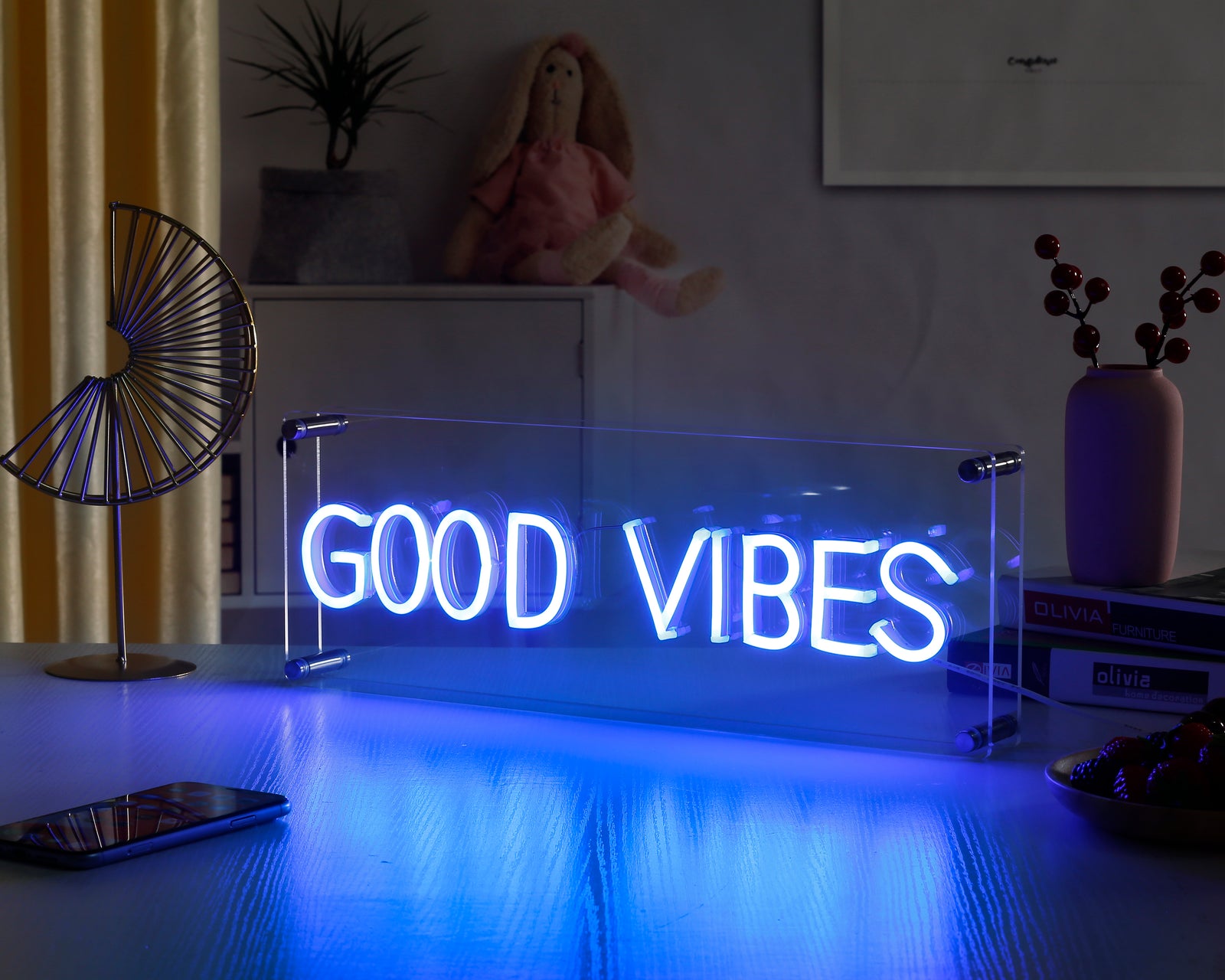 Glowing 'Good Vibes' blue neon desk sign resting on a light wood grain surface.