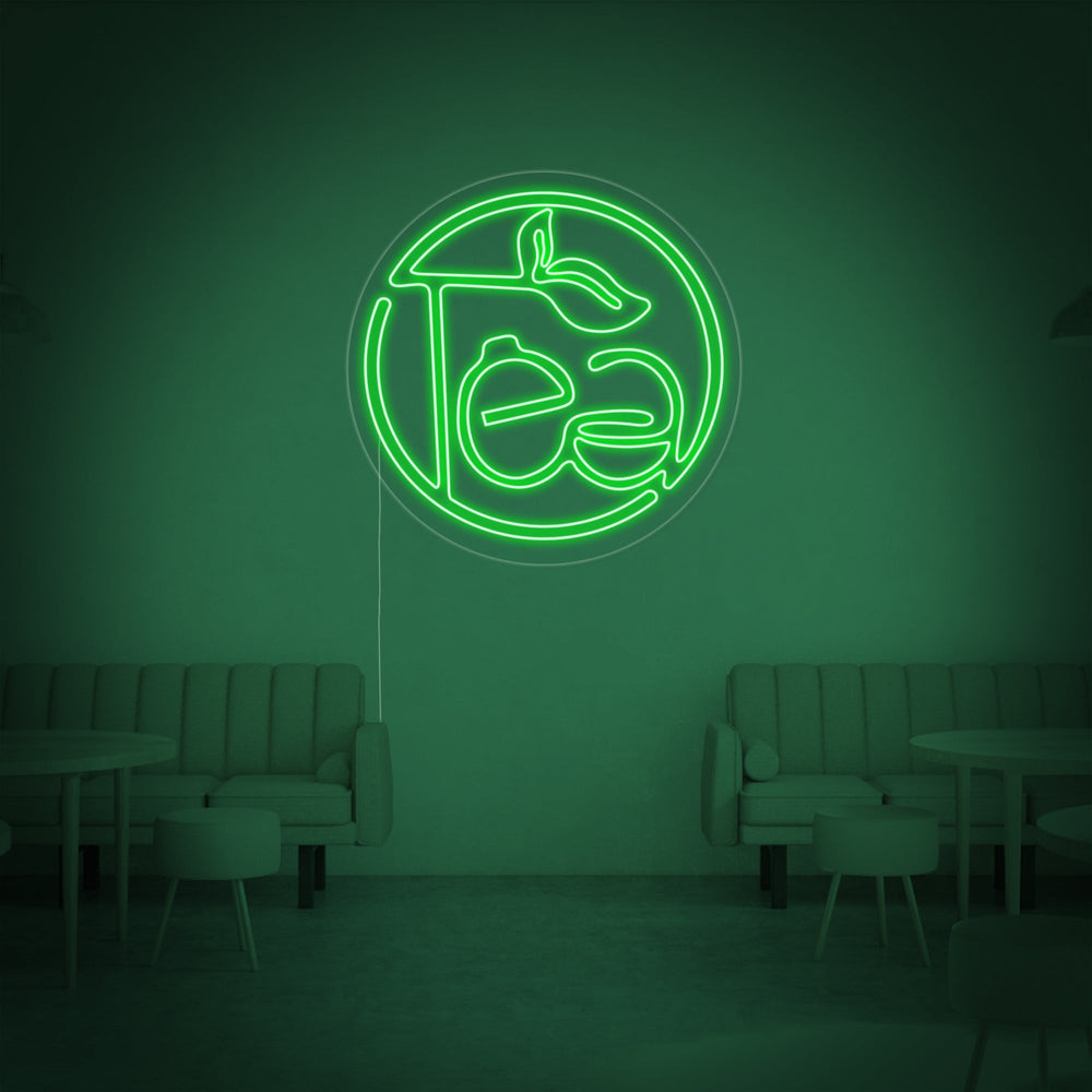 Close-up view of the 'Green Tea' neon sign, showing the detailed craftsmanship of the glowing green tubes and clear backer, illuminating a stylish, modern room.