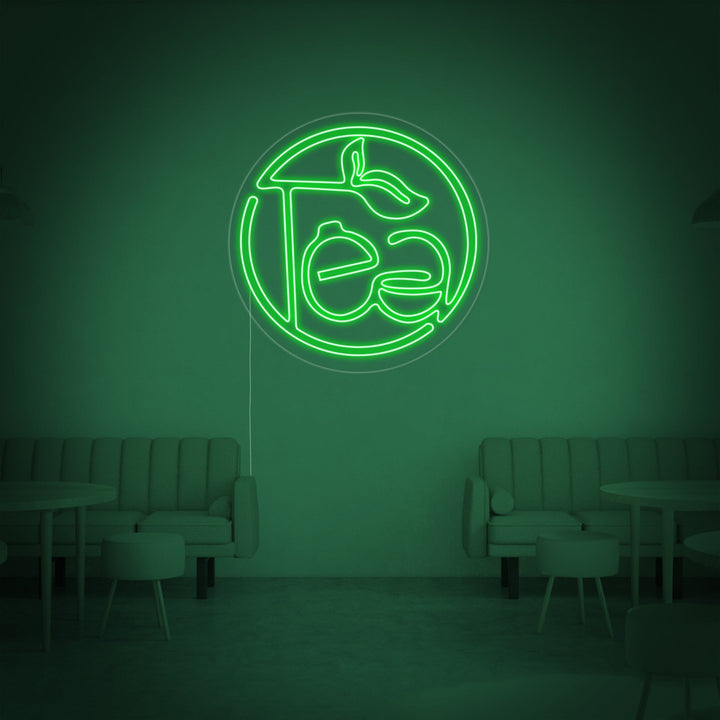 Close-up view of the 'Green Tea' neon sign, showing the detailed craftsmanship of the glowing green tubes and clear backer, illuminating a stylish, modern room.