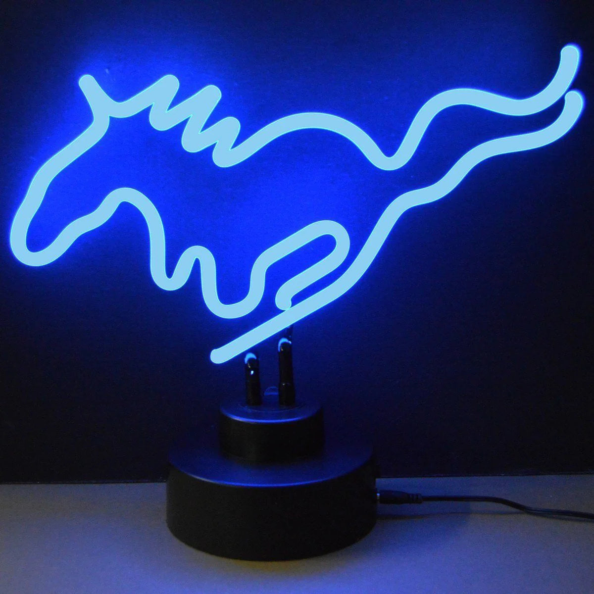 Handcrafted neon sign depicting a galloping horse in glowing warm white, mounted on a dark wooden base on a rustic table with a stone wall background.