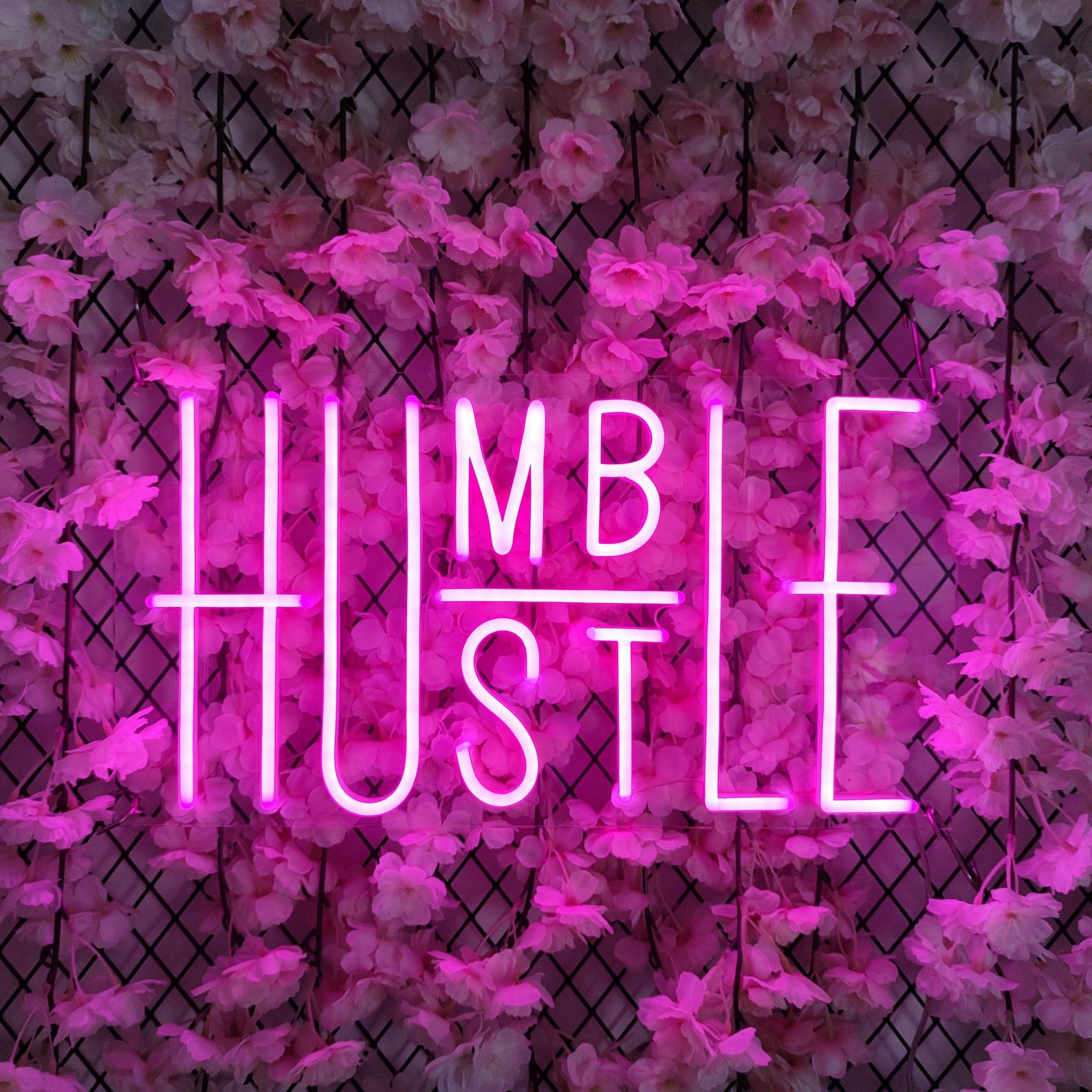 Humble Hustle neon sign glowing white on a wall with white floral lattice panels