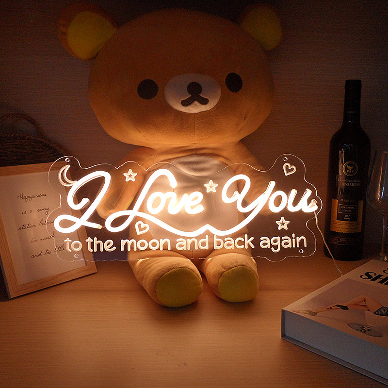 Side view of I Love You To The Moon And Back Again neon sign illuminating a cozy living space above a grey sofa.