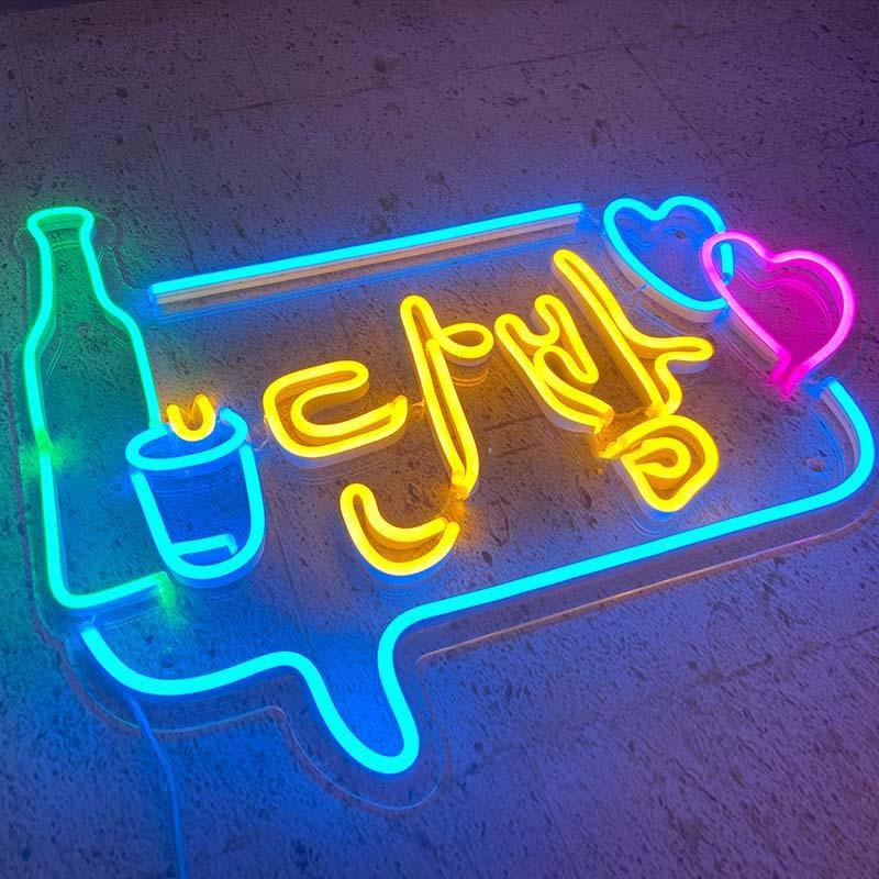 A real, glowing 'ITAEWON CLASS' Korean neon sign featuring vibrant pink, blue, yellow, and green colors, mounted on an acrylic backing plate and displayed on a textured floor.