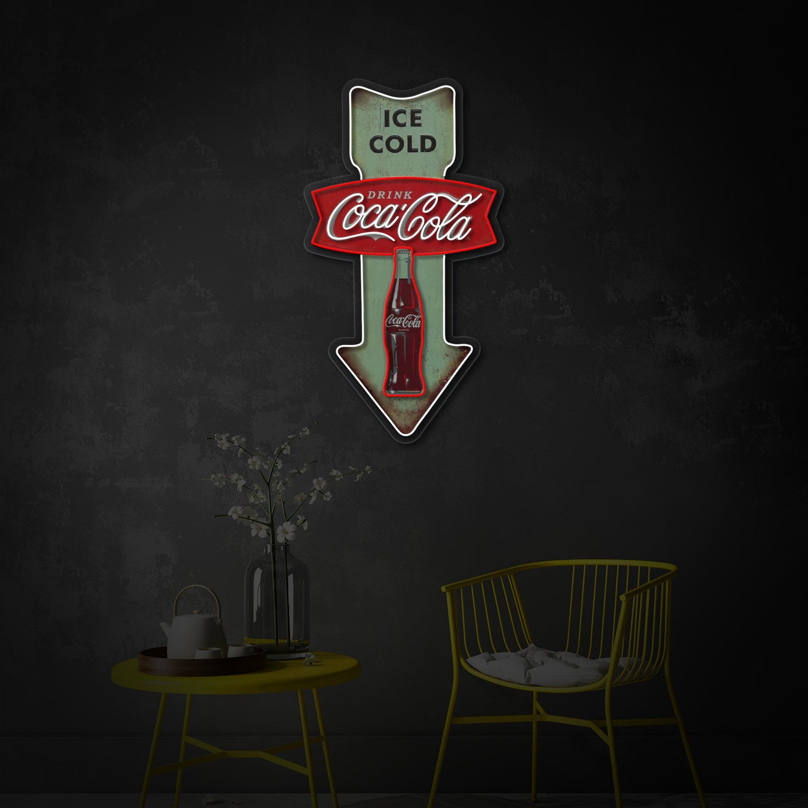 The Ice Cold Cola Vintage Diner Arrow neon sign displayed on a wall above a wooden table and chair, creating a nostalgic atmosphere in a room setting.