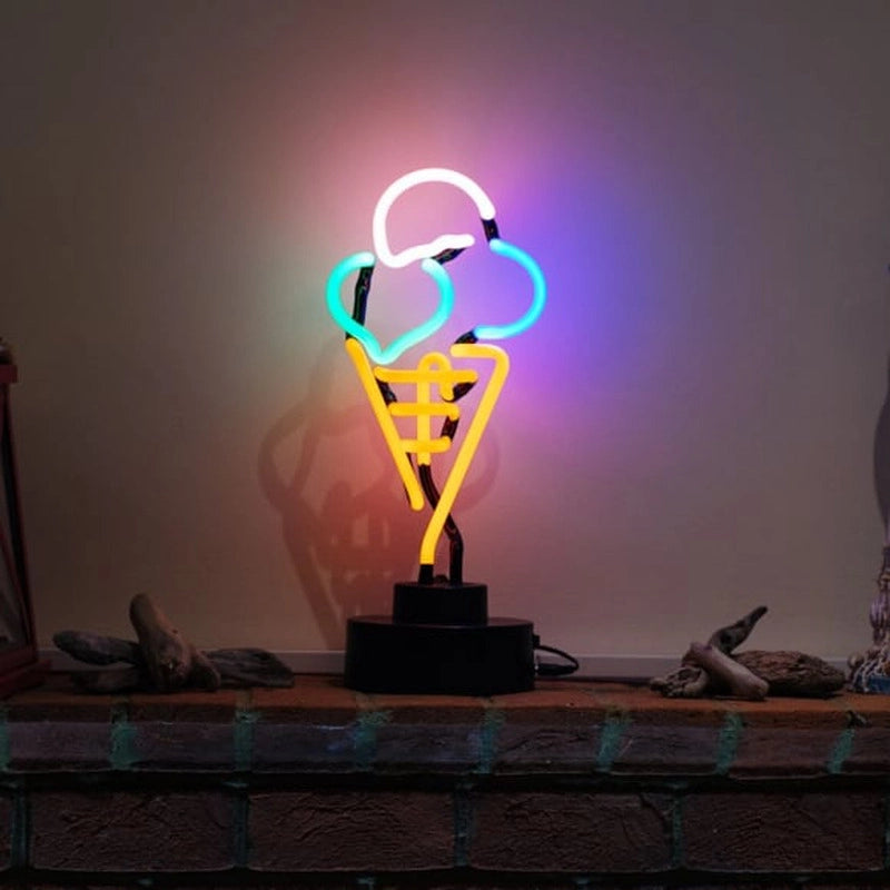 A real neon sign shaped like an ice cream cone on a physical base, glowing brightly on a table against a textured wall.