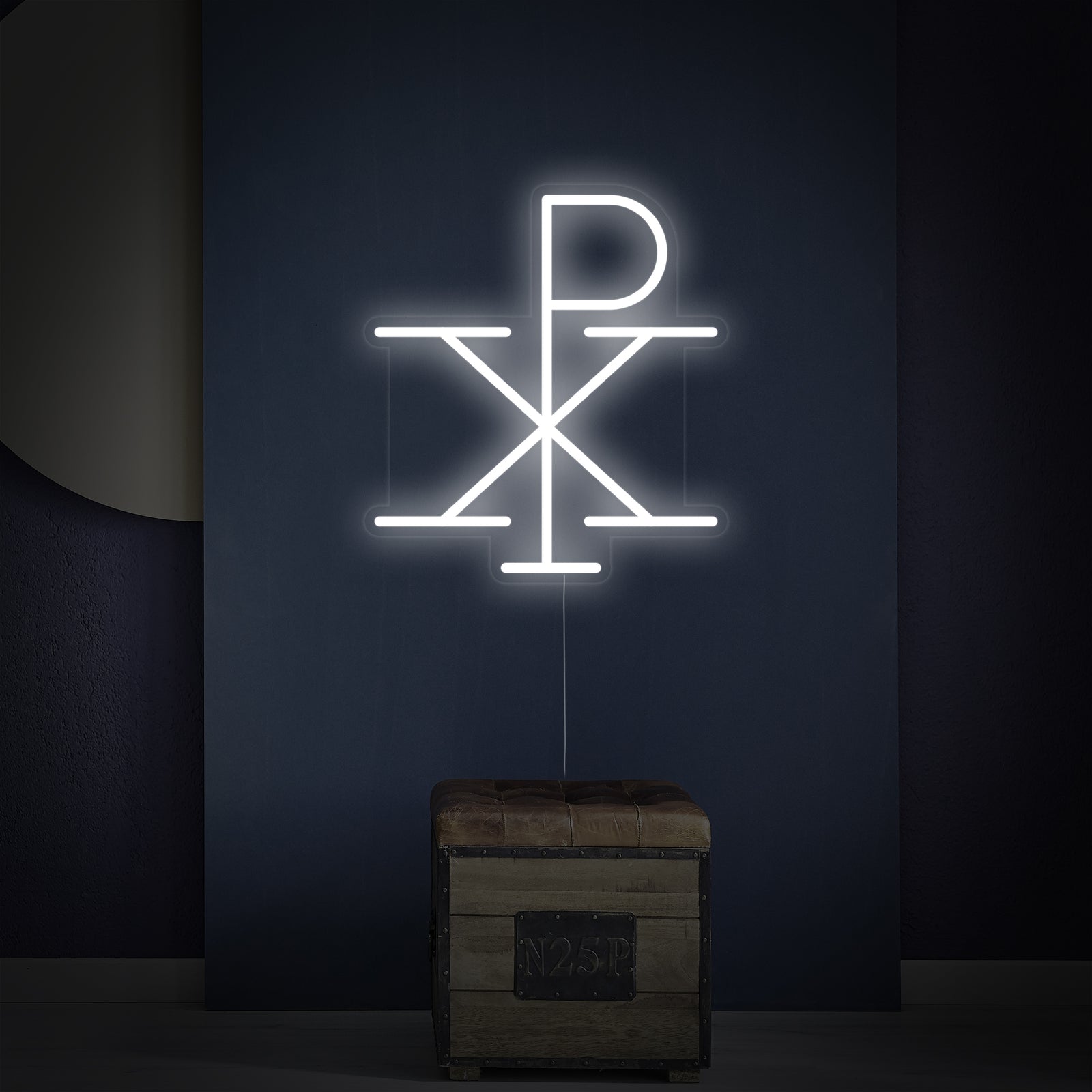 The 'Jesus Monogram of Christ Chi Rho' neon sign shown on a wall above a small wooden shelf with decorative items.