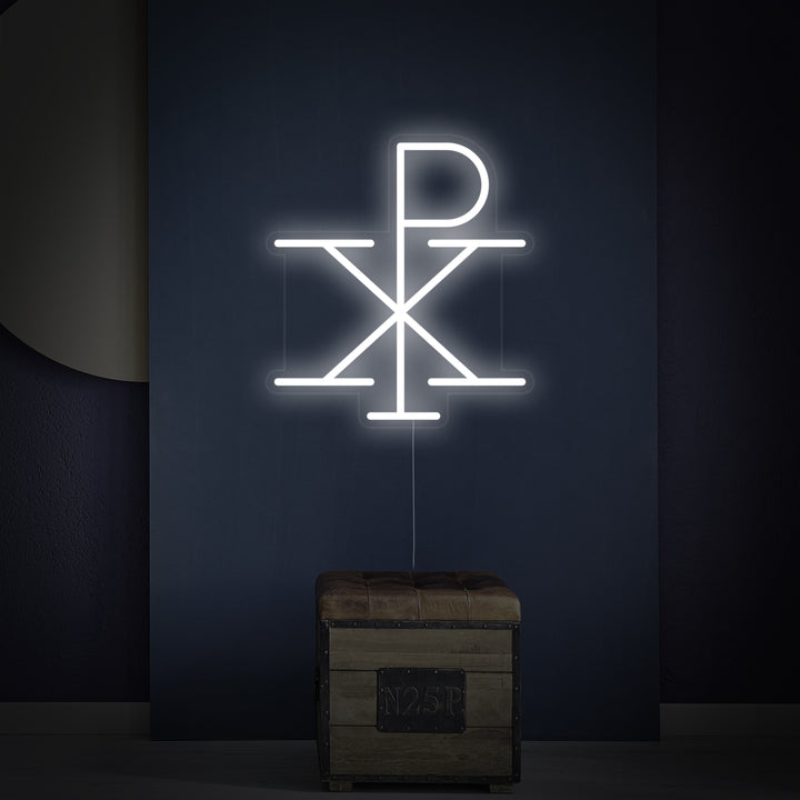 The 'Jesus Monogram of Christ Chi Rho' neon sign shown on a wall above a small wooden shelf with decorative items.