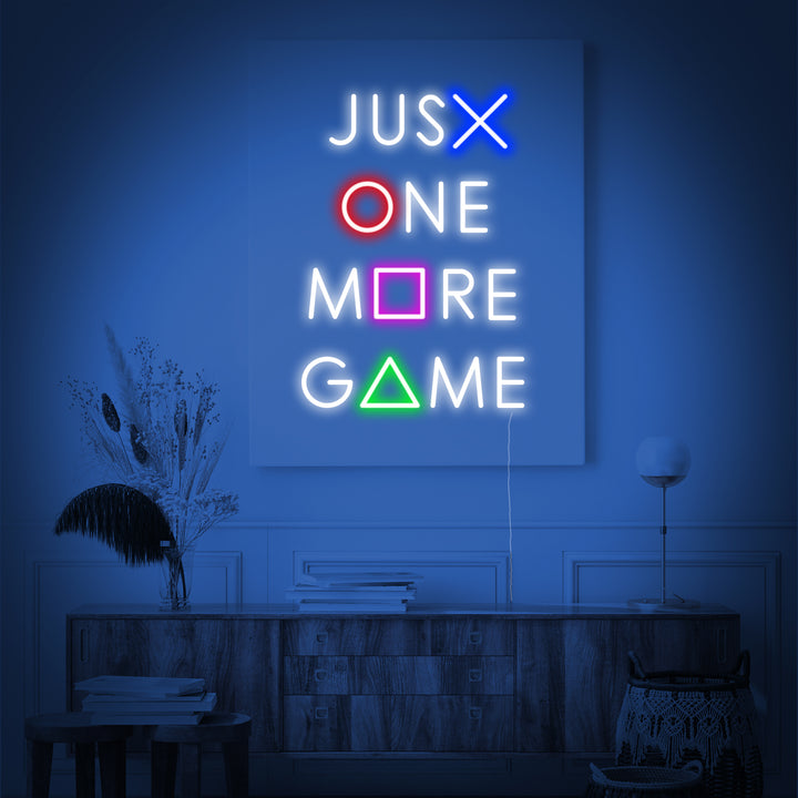 A close-up view of the 'Just One More Game' neon sign showing the distinct glowing tubes against a dark textured wall background.