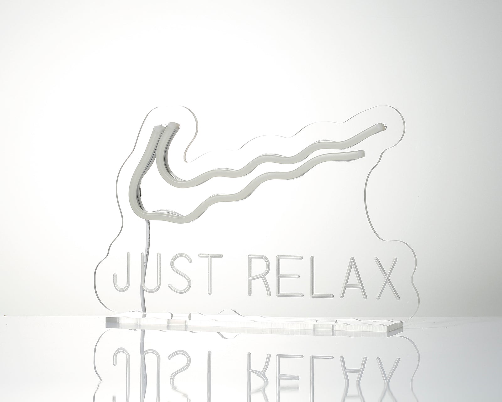 Just Relax custom neon sign glowing blue script mounted on a transparent acrylic base with stand on a light grey background.