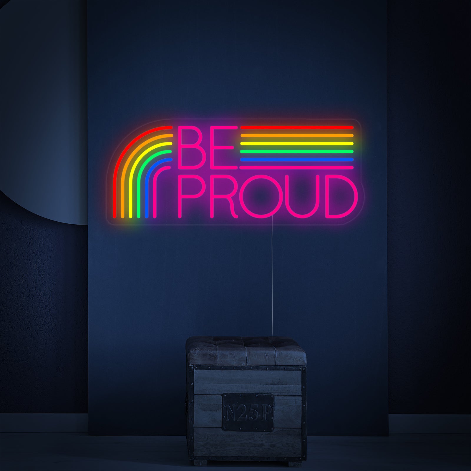 A glowing 'LGBT Be Proud' rainbow neon sign with a clear acrylic backing, casting a colorful light on a wall.