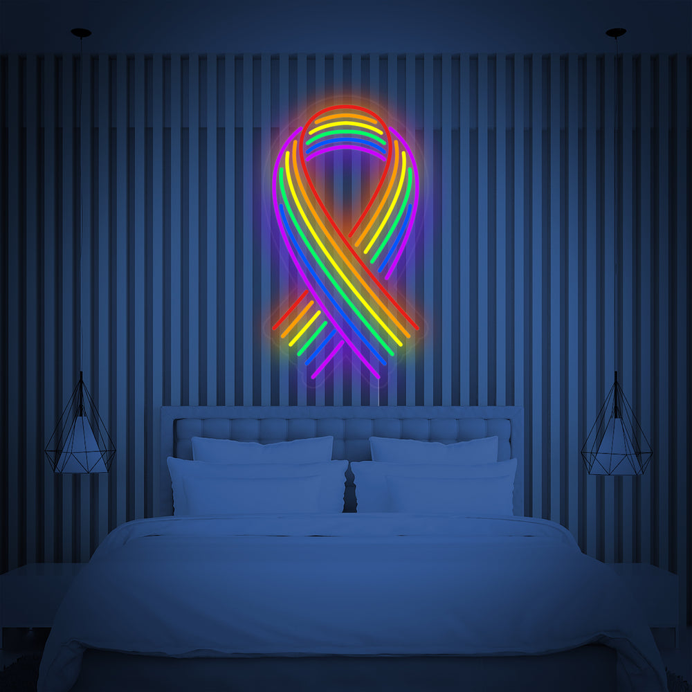 A lit 'LGBT Ribbon Rainbow' neon sign mounted on a bedroom wall above a bed, illuminating the surrounding space.