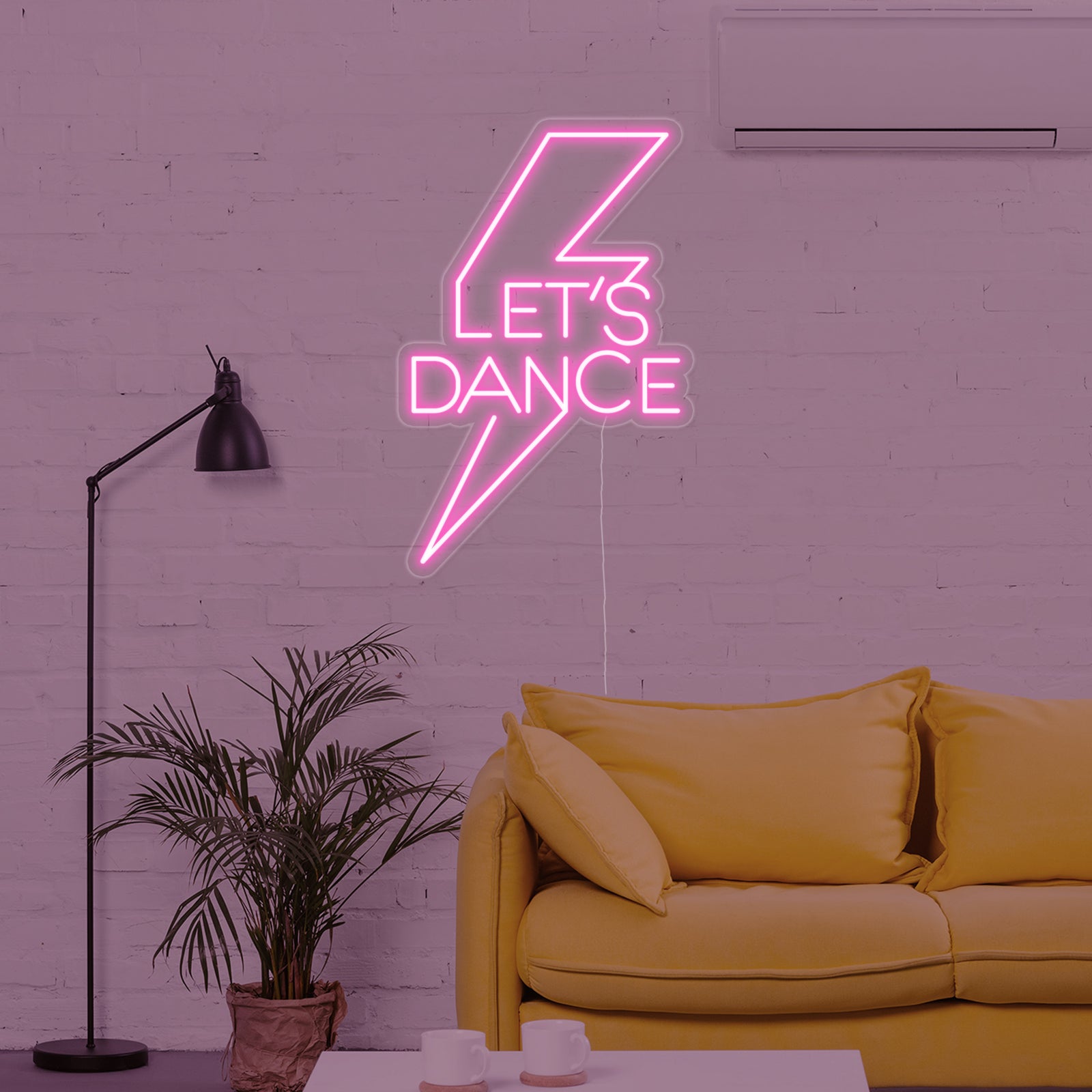 Close-up of the 'Lets Dance' neon sign with clear acrylic backing, casting a pink glow in a rustic room.