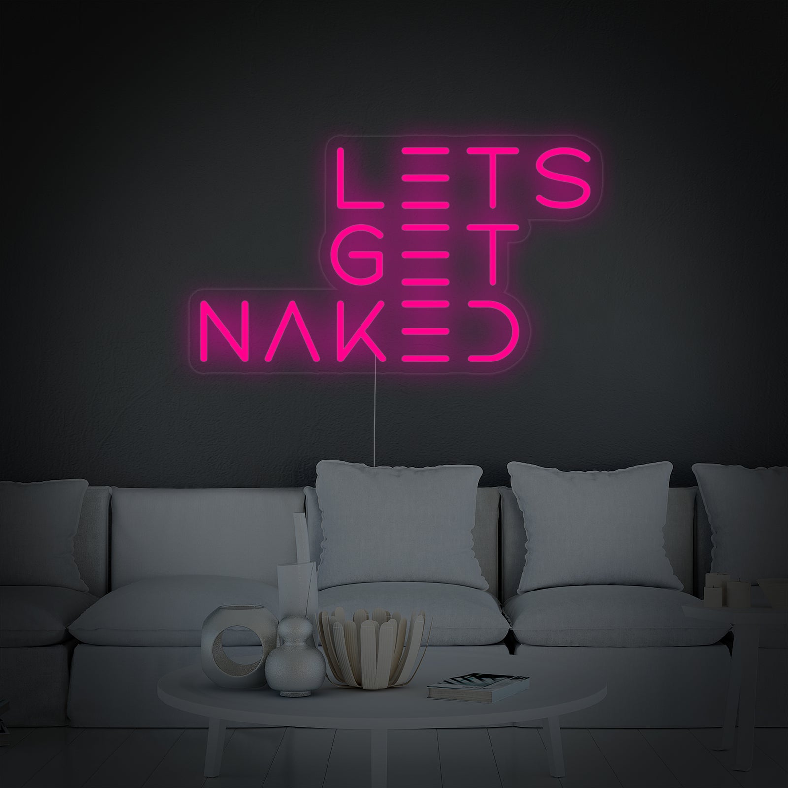 A close-up photograph of the "Let's Get Naked" bathroom neon sign, illuminated in white, clearly showing the script font, acrylic backing, and mounting hardware.