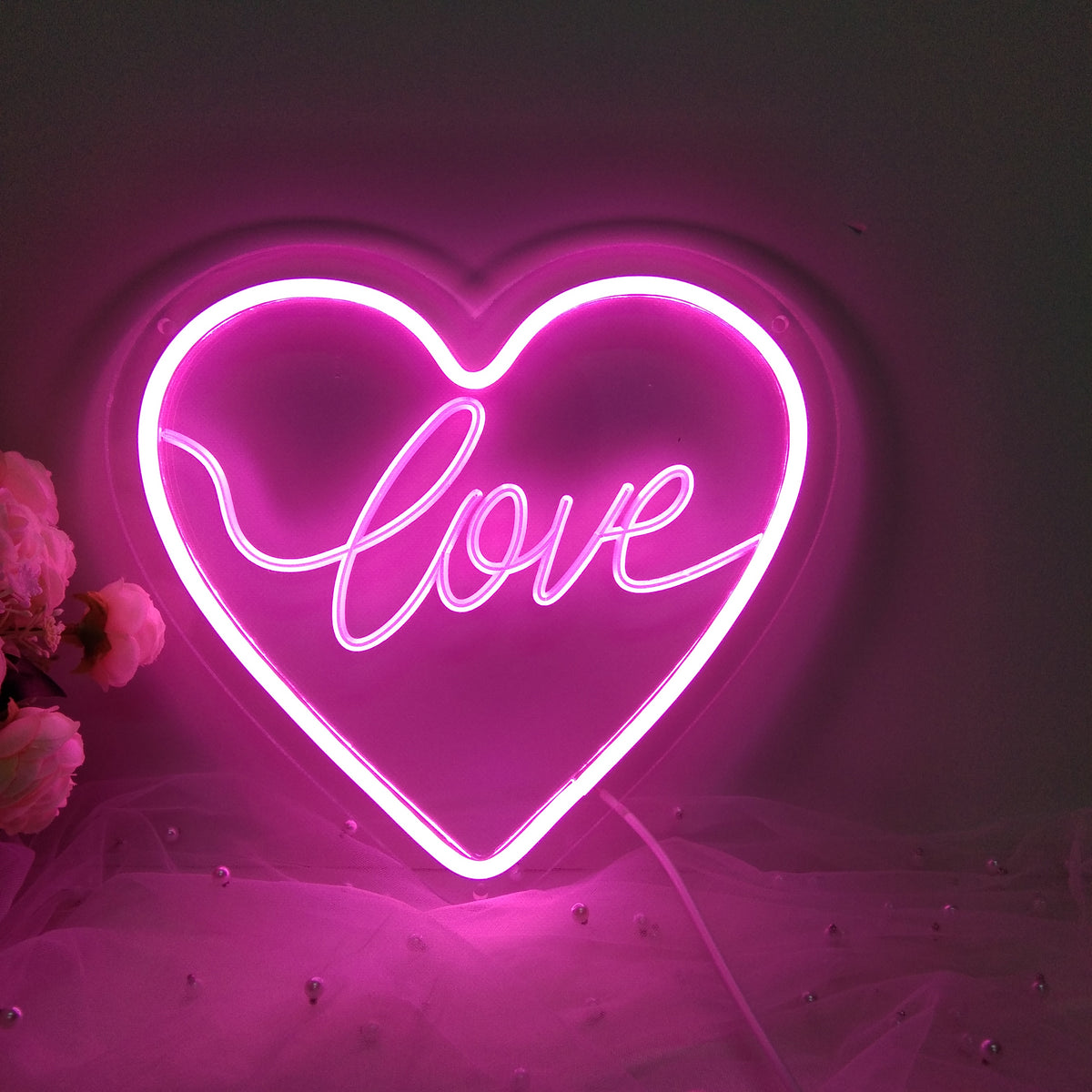 Illuminated mini neon sign in a heart shape, casting a pinkish light on a wooden surface.