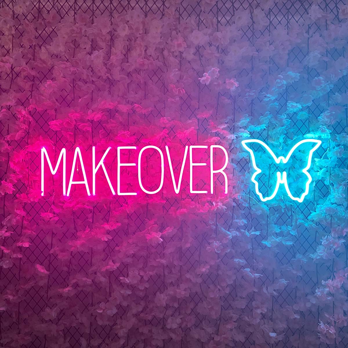 A illuminated butterfly and 'Makeover' neon sign mounted on a floral wall background.