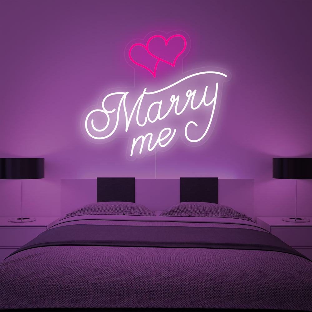 A glowing red "Marry Me Hearts" neon sign featuring two intertwined hearts above a plush white bed.