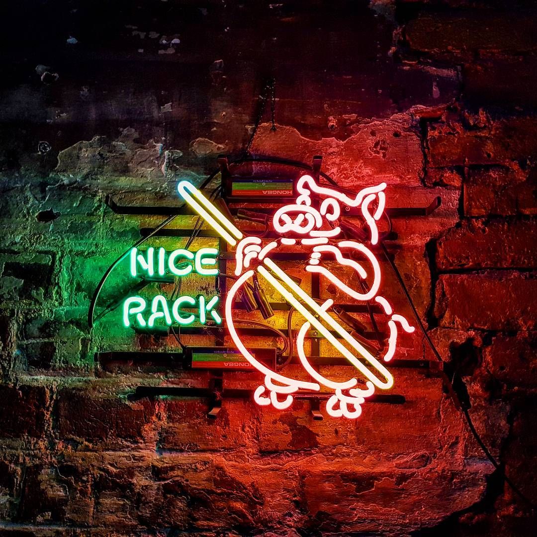 The 'Nice Rack' neon sign hanging on a distressed brick wall, illuminating a billiards-themed room.