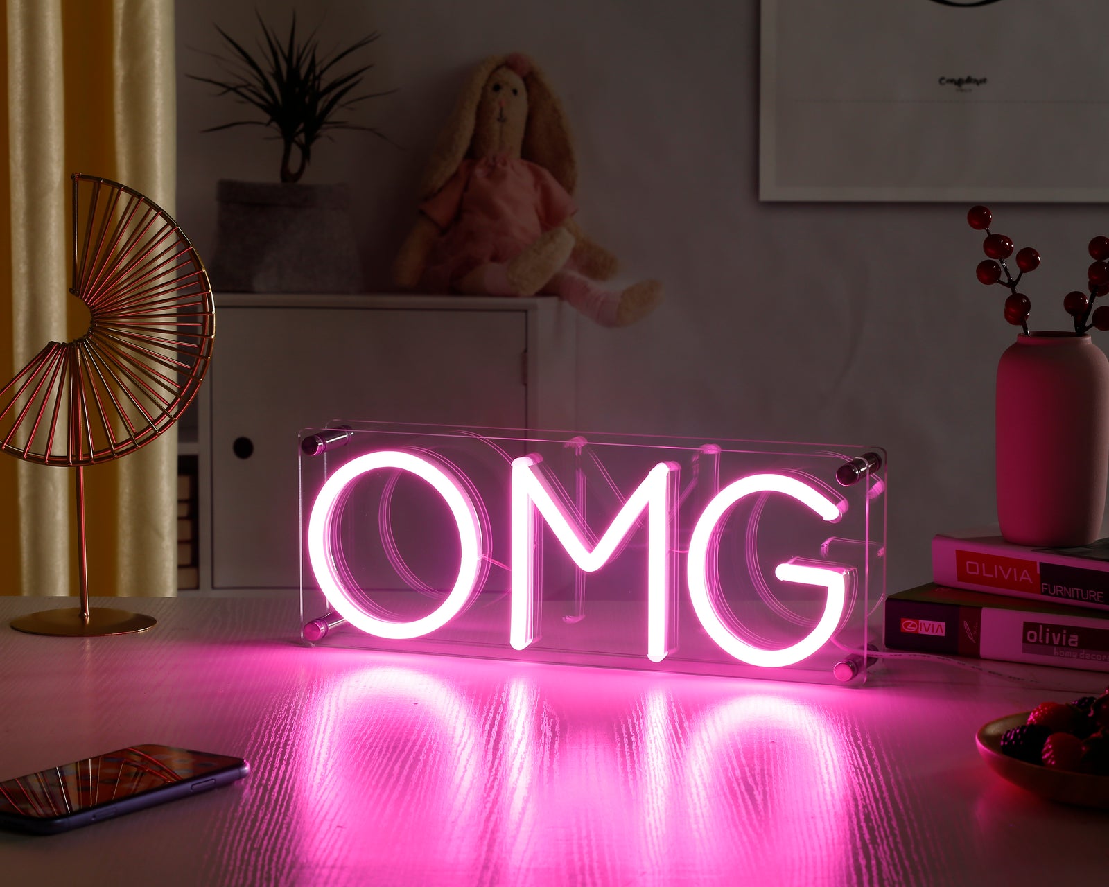 Glowing 'OMG' neon sign on clear acrylic block with chrome corner mounts, placed on a surface.