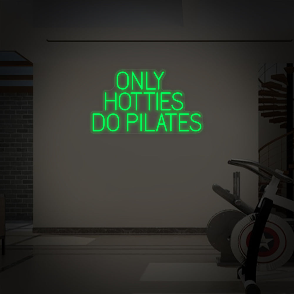 A close-up view of the glowing pink neon tubes spelling out 'Only Hotties Do Pilates' on a clear acrylic backing.