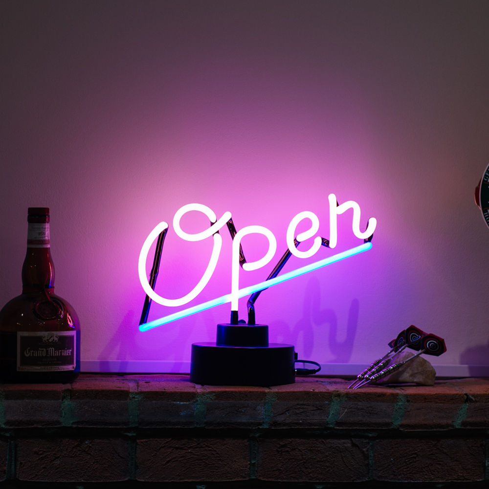 A glowing pink neon sign that reads "OPEN" sitting on a rustic brick ledge with scattered objects.