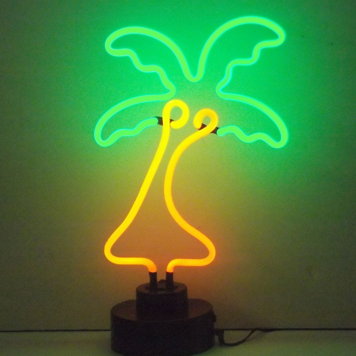 A glowing green and yellow palm tree glass neon table sign lit up on a black base.