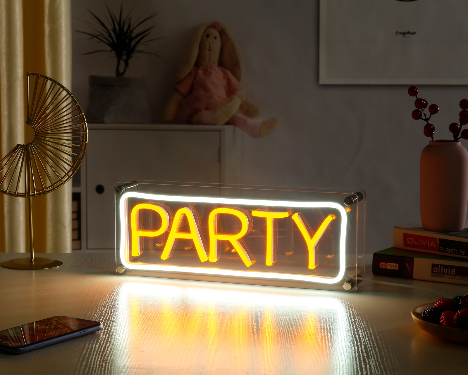 Handcrafted 'Party' neon sign on a clear acrylic stand, glowing brightly on a wooden desk with visible power cord and inline switch.