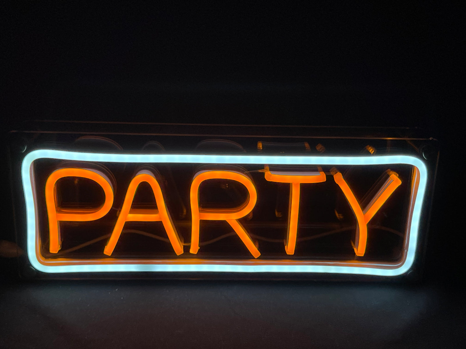 Close-up photograph of the 'Party' neon text in a warm glow, mounted on an acrylic panel with chrome standoff hardware.