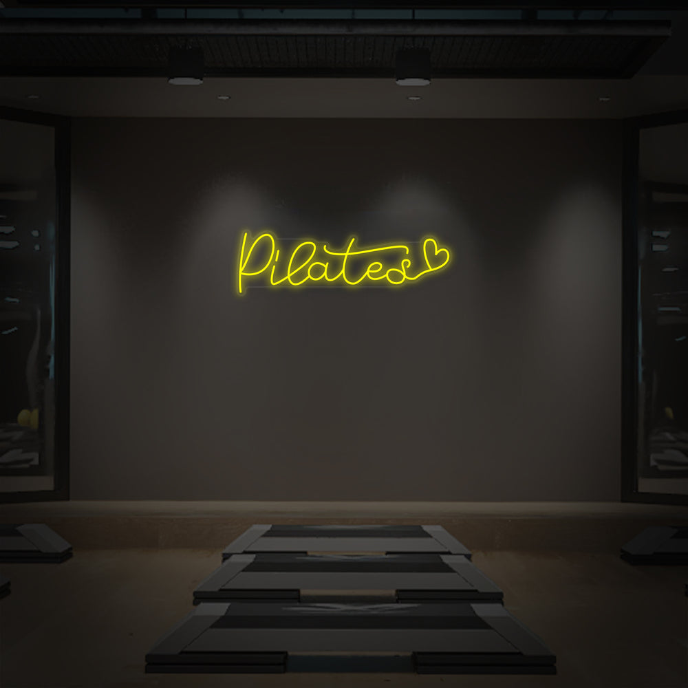 A flat-lay illustration or graphic mockup of the "Pilates Heart" neon sign on a simple textured wall background.