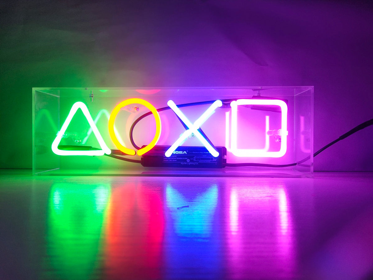 Geometric gaming controller design neon sign in an acrylic box, sitting on a table with a warm, ambient glow.