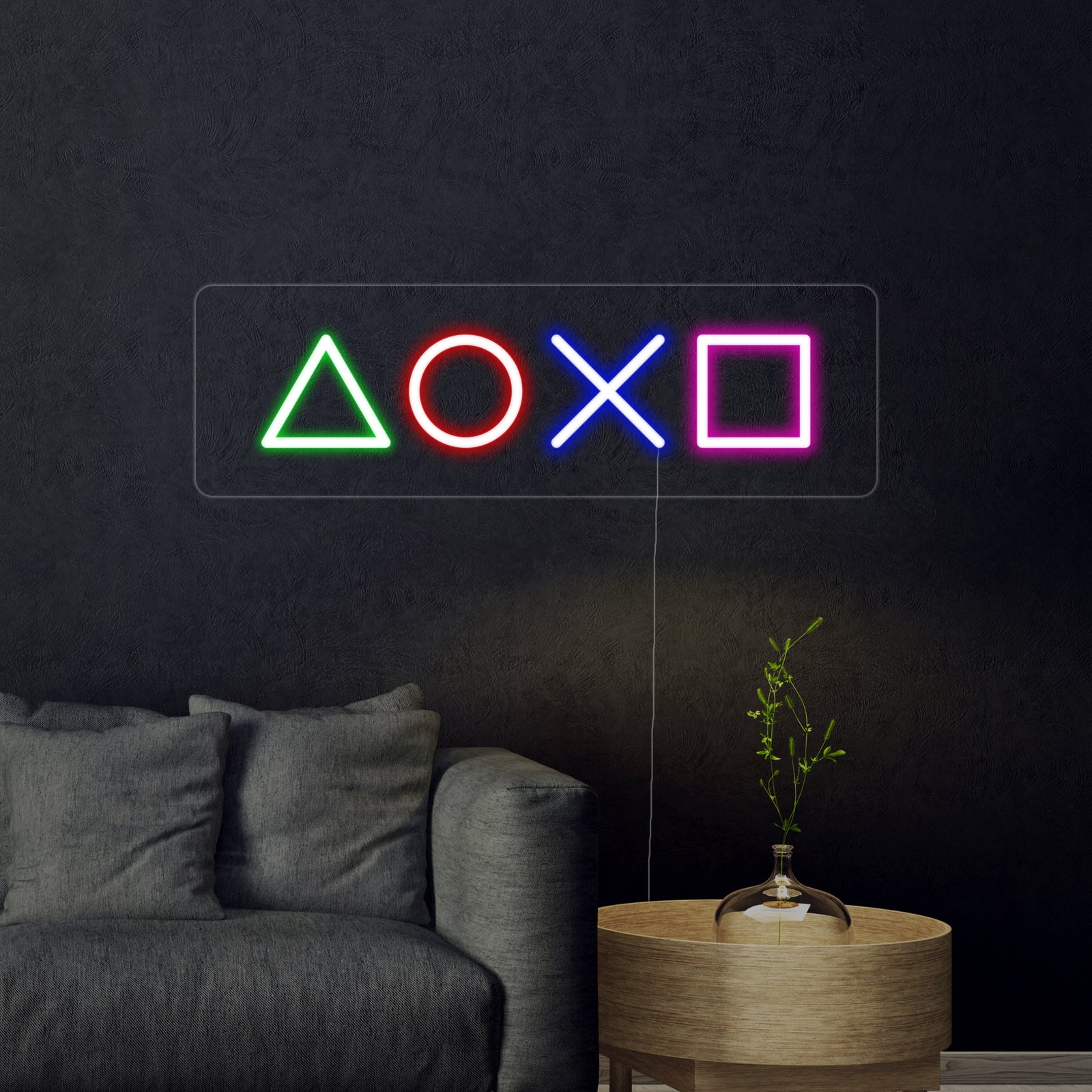 Close-up photograph of the 'Play Gaming Station Geometry' neon sign, featuring the word 'PLAY' in a stylized font above four distinct glowing geometric shape icons, mounted on a clear backboard against a dark wall.