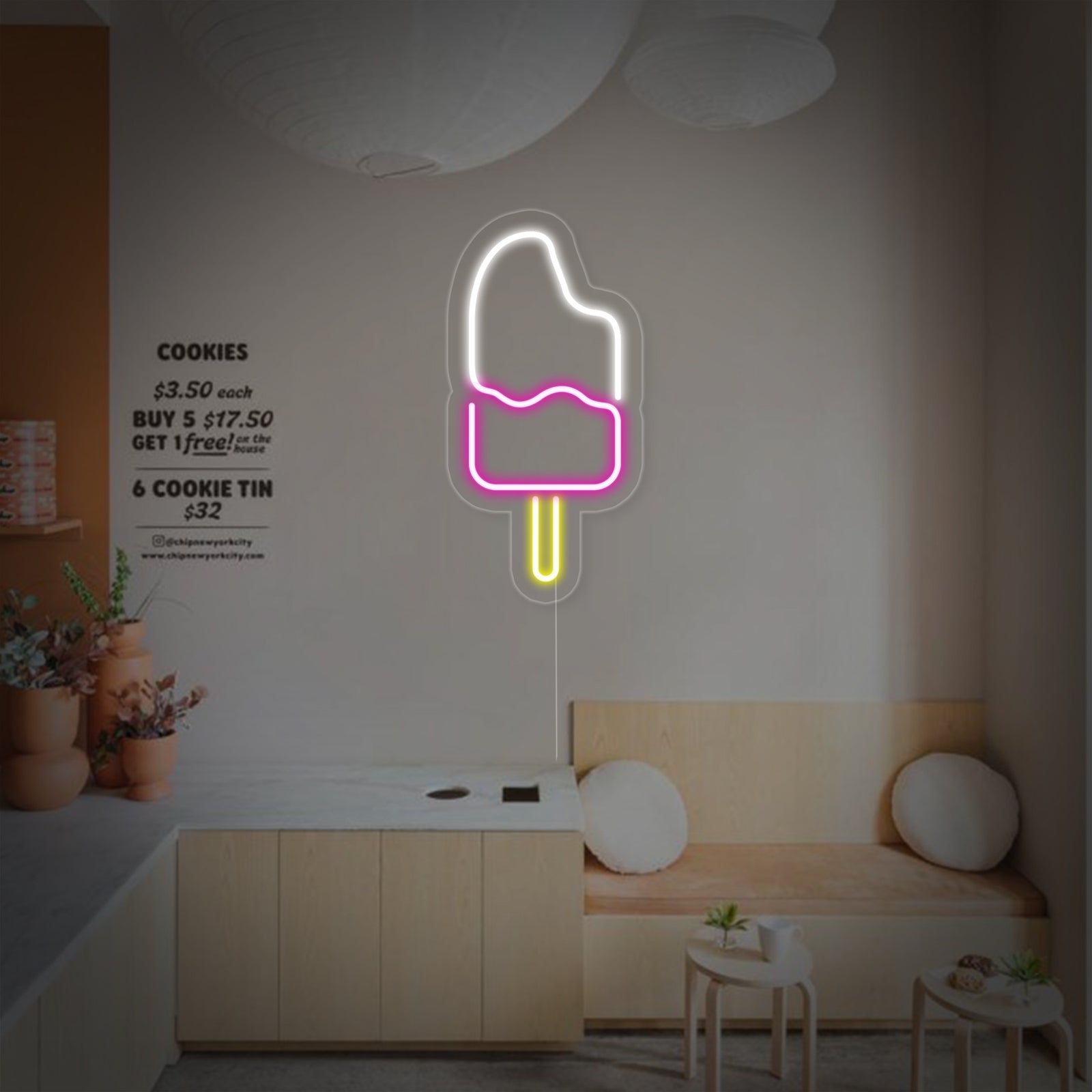 A vibrant red and blue neon sign shaped like a popsicle mounted on a textured teal wall with an industrial-style light fixture.