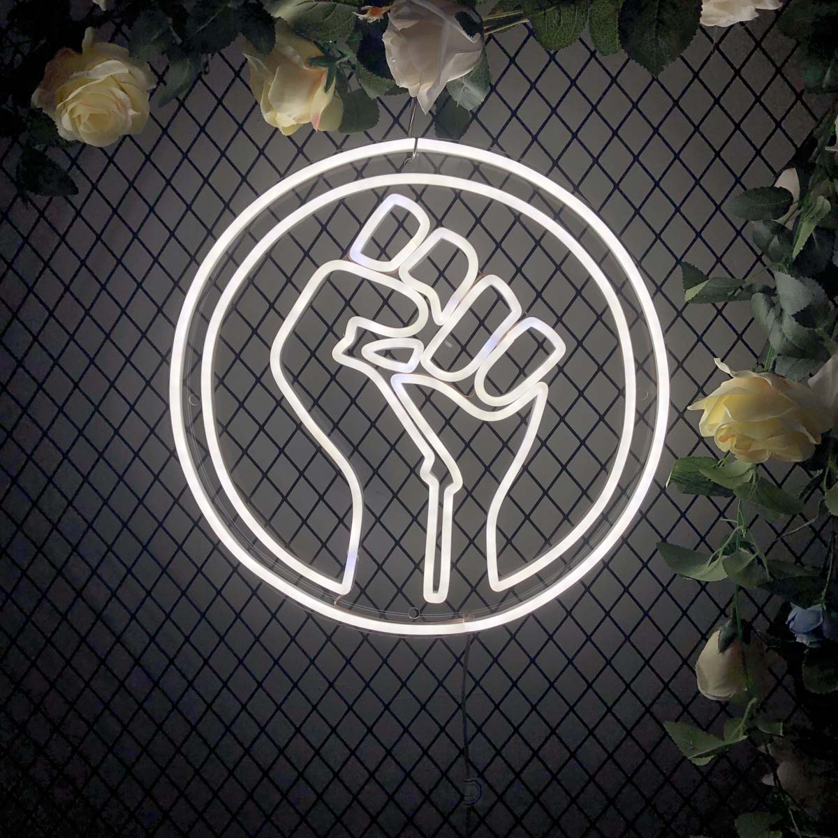 A glowing 'Power Hand' neon sign featuring a fist with lightning bolts, mounted on a mesh background with plants.