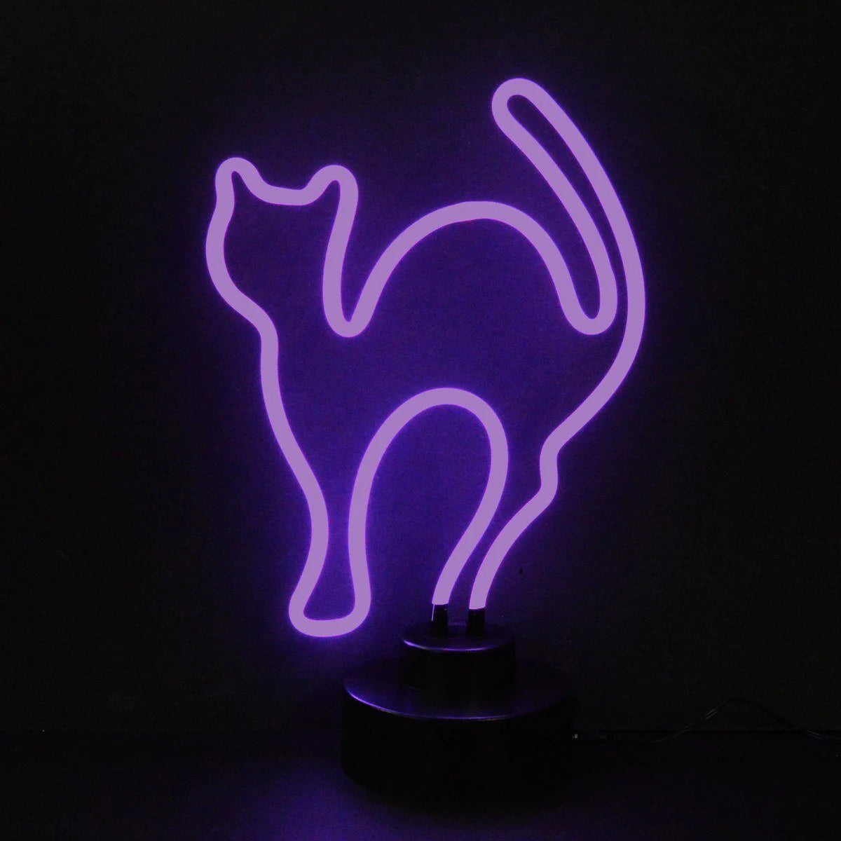 A glowing purple neon sign shaped like a cat sitting on a table next to a stack of books.