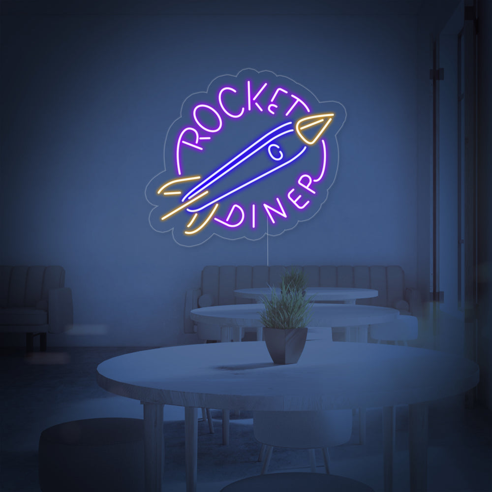 Closer view of the illuminated ROCKET DINER neon sign on a textured wall, showing detailed neon tube work and design.